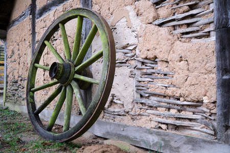 Old wagon wheel leaning up against an old historic rustic mud or daub and timber frame building with weathered walls and exposed wood framework in a closeup viewの写真素材