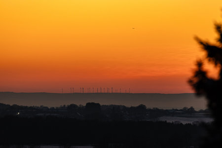 Wind turbines and a lonely airplane against a beautiful sunsetの写真素材