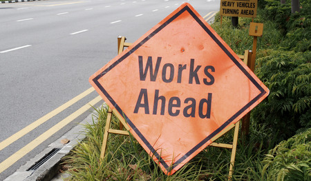 Work ahead signage along the street with plants backgroundの写真素材