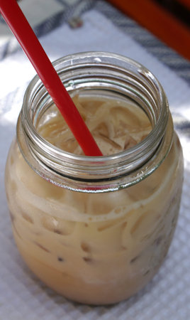 Iced coffee in the glass jar and red straw with nature background