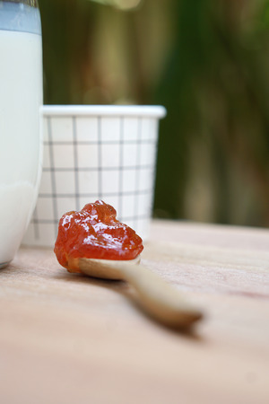 Timber spoon of strawberry jam with milk jar and a cup of ice cream with nature backgroundの写真素材