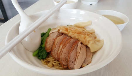 Dry egg noddle with duck meats and shrimp dumpling on white bowlの写真素材