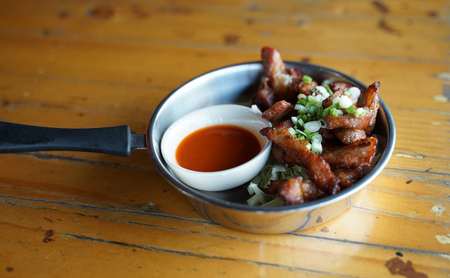 Deep fried pork serving with chili sauce in the small cooking pan on timber tableの写真素材