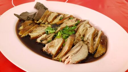 Asian style fresh sliced duck meat strewed with special black soy sauce on pink plate with red backgroundの写真素材