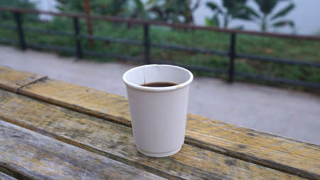 Hot coffee in white paper cup on rustic timber table with nature backgroundの写真素材