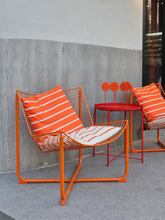 Wire metal outdoor furnitire in bright orange with stripe cushion in orange and white on grey floor outdoorの写真素材