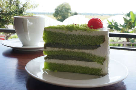 A cup of coffee in a white cup with colorful cream pandan cake on wooden background.の写真素材