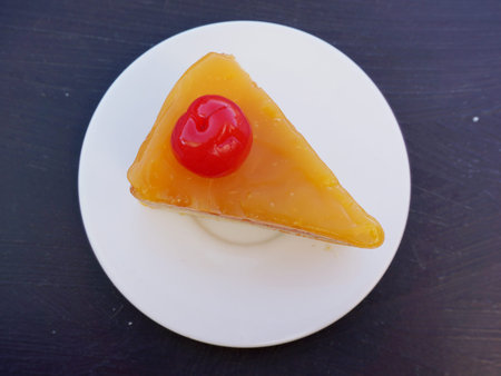Colorful orange layer cake decorated with cherry on wooden background, close up