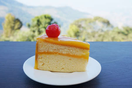 Colorful orange layer cake decorated with cherry on wooden table in natural background, close upの写真素材
