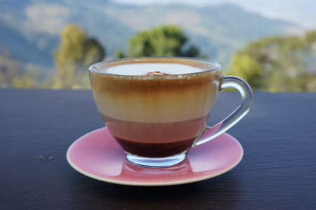 A cup of layer coffee in a glass cup on a dark wood table in natural background.の写真素材