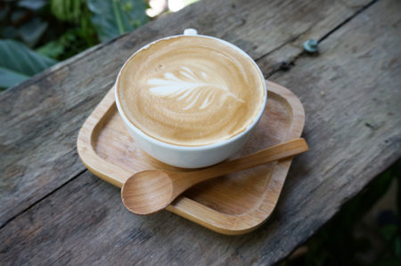 A cup of coffee in a white cup with wooden teaspoon on wood table.