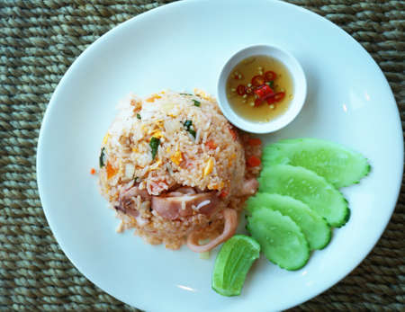 Asian food, Thai food, squid fried rice with cucumber and lime in a white plate on a tableの写真素材