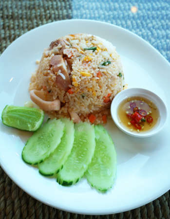 Asian food, Thai food, squid fried rice with cucumber and lime in a white plate on a tableの写真素材