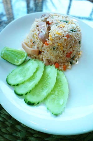 Asian food, Thai food, squid fried rice with cucumber and lime in a white plate on a tableの写真素材