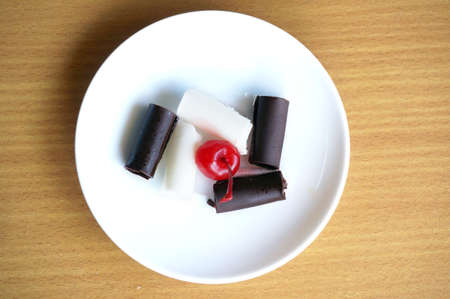 Various sweet topping, red cherry, chocolate and white chocolate on a white plate on wooden backgroundの写真素材