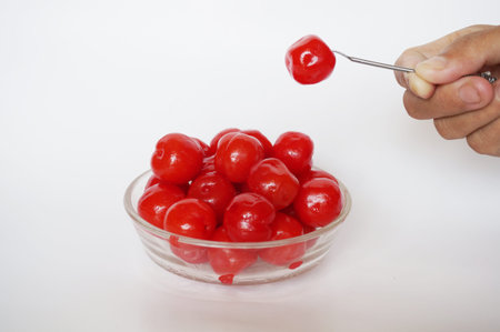 Hand pick up maraschino cherries in a glass bowl with a silver fork isolated on white backgroundの写真素材