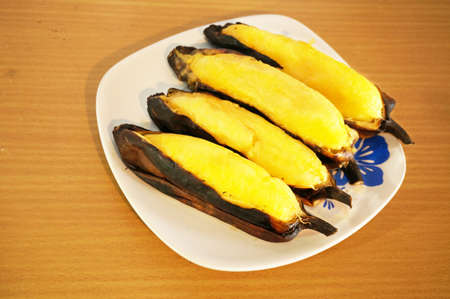 Asia - Asian food, Thai dessert, delicious grilled Silver Bluggoe banana in yellow color with black banana peel on wooden table isolated on white backgroundの写真素材