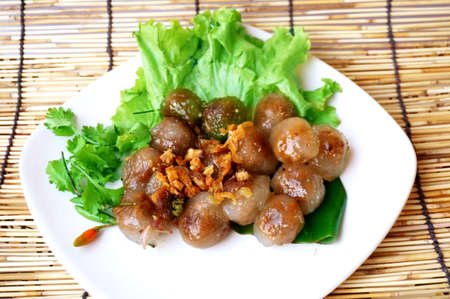 Asia - Asian eating food, Thai food, Tapioca pork balls - steamed tapioca balls with pork filling served with lettuce, fried garlic and chilli padi or Thai pepper ( Bird Chilli ) on white plate on rattan curtain backgroundの写真素材