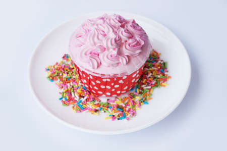 Colorful cream strawberry cupcake decorated with sugar topping on white plate isolated on white backgroundの写真素材