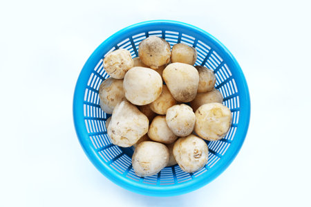 A photo of fresh straw mushrooms ( Volvariella volvacea ) in blue basket isolated on white...
