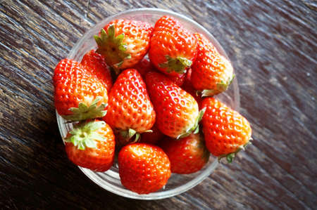Close up of photo of very fresh harvested strawberries in glass bowl on wooden backgroundの写真素材