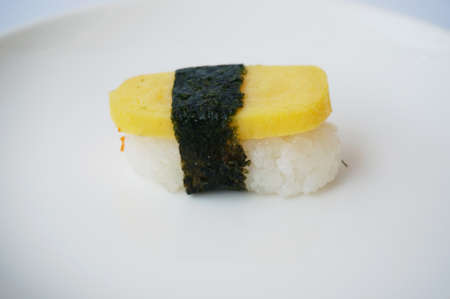 Asia - Asian eating food, Japanese food, sweet egg roll sushi with seaweed on white plate isolated on white background, close up.の写真素材