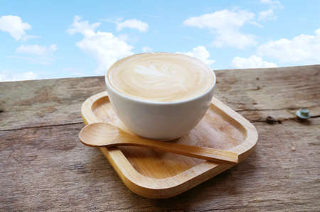 A cup of coffee in a white cup with wooden teaspoon on a wood table wiht natural background.の写真素材