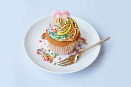 A photo of colorful cream cupcake decorated with heart shape sugar topping with fork on white plate isolated on white background, close upの写真素材
