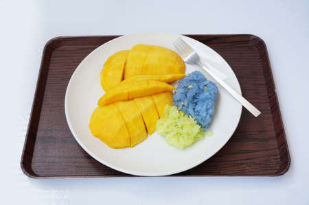 Asia - Asian eating food, Thai dessert, Sticky rice in coconut cream with sweet ripe mango, with fork on white plate and wooden tray isolated on white background, close upの写真素材