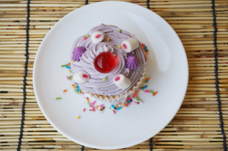 Colorful cream butter cupcake decorated with sugar and jelly ball topping on white plate on rattan curtain backgroundの写真素材