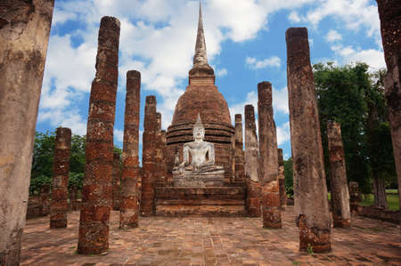 A photo of Buddha sitting in front of a pagoda, with ruin of stone pillars, is a World Heritage at Sukhothai Historical Park, Sukhothai, Thailandの写真素材