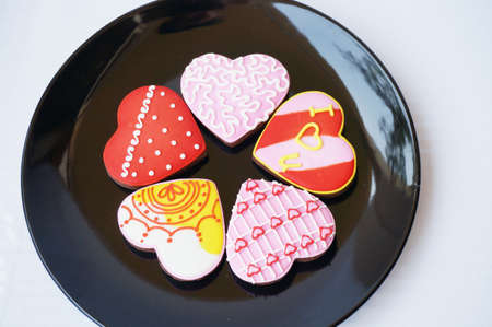 Love Heart Cookies: Chocolate cookies decorated with various color of sugar topping on black plate isolated on white background.の写真素材