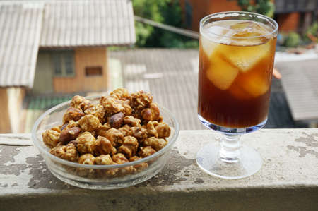 A photo of caramel popcorn on glass blow and cola on champagne glass on balcony of an old building with natural background, close upの写真素材