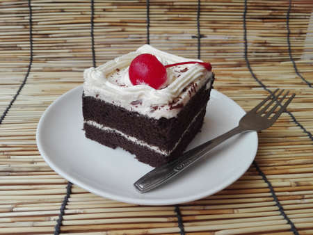 A photo of colorful chocolate black forest cake decorated with cherry on rattan curtain background, close upの写真素材
