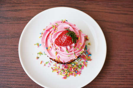 A photo of colorful cream strawberry cupcake decorated with sugar topping on white plate isolated on white background, close upの写真素材