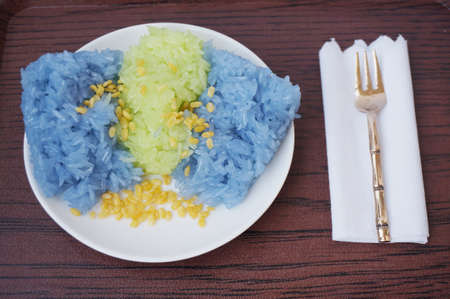 Asia - Asian eating food, Thai dessert, Sticky rice in coconut cream with fork on white plate on wooden background, close upの写真素材