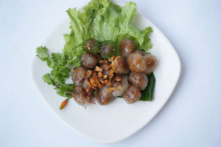 Asia - Asian eating food, Thai food, Tapioca pork balls - steamed tapioca balls with pork filling served with lettuce, fried garlic and chilli padi or Thai pepper ( Bird Chilli ) on white plate on rattan curtain background, close upの写真素材
