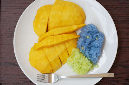 Asia - Asian eating food, Thai dessert, Sticky rice in coconut cream with sweet ripe mango, with fork on white plate on wooden background, close upの写真素材