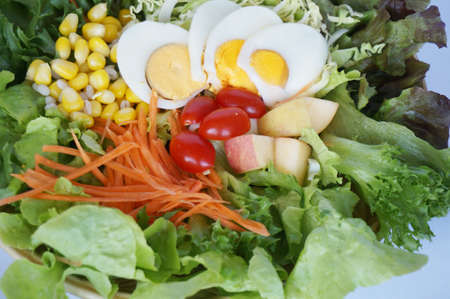 A photo of fresh vegetables prepare for salad, corn, tomatoes, apple, cabbage, lettuce with boiled eggs isolated on white background, close upの写真素材
