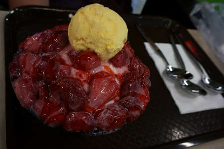 Asia-Asian eating food, Bing su: Korean shaved ice dessert with sweet toppings, strawberry and vanilla ice-cream in black ceramic bowl on the table, close upの写真素材