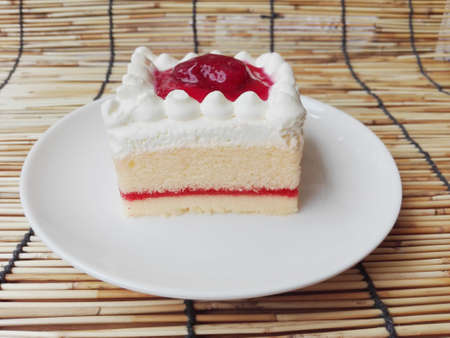 Colorful vanilla cream cake decorated with strawberry topping on rattan curtain backgroundの写真素材