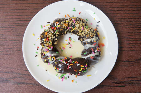 A photo of chocolate donut with sugar topping on white plate on wooden background, close upの写真素材