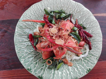 Asia-Asian eating food: Crispy shrimp with sweet tamarind sugar sauce. Decorated with fried chili and Kaffir lime leaf, crispy onion on a plate on wooden background, close upの写真素材