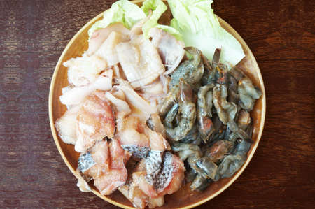 Raw foods: Fresh squid, white leg shrimp or pacific white shrimp (Litopenaeus vannamei, formerly Penaeus vannamei) and fish with chinese cabbage on plate on wooden background, close upの写真素材