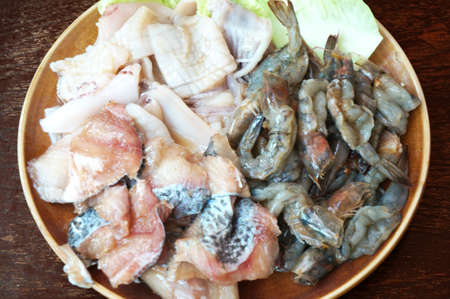 Raw foods: Fresh squid, white leg shrimp or pacific white shrimp (Litopenaeus vannamei, formerly Penaeus vannamei) and fish with chinese cabbage on plate on wooden background, close upの写真素材
