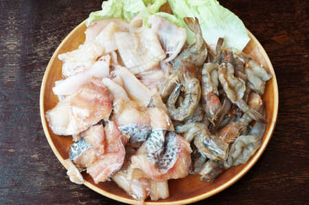 Raw foods: Fresh squid, white leg shrimp or pacific white shrimp (Litopenaeus vannamei, formerly Penaeus vannamei) and fish with chinese cabbage on plate on wooden background, close upの写真素材