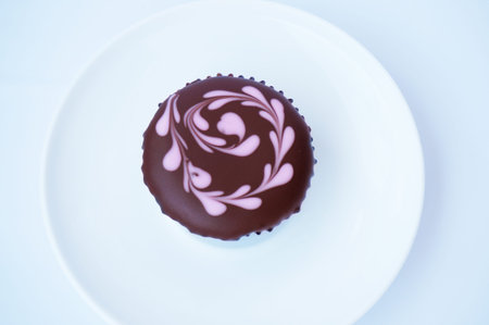 A photo of chocolate cupcake with topping on white plate isolated on white background, close up