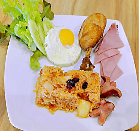 Asian food, Thai food, American Fried Rice with cucumber, chicken, ham and sausage on white plate on wooden backgroundの写真素材