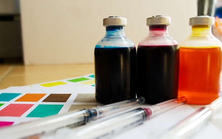 Bottle of ink printer has three colors. Colors is red, yellow and blue with syringe on colored paper.の写真素材