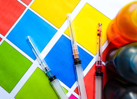 Bottle of ink printer has three colors. Colors is red, yellow and blue with syringe on colored paper.の写真素材